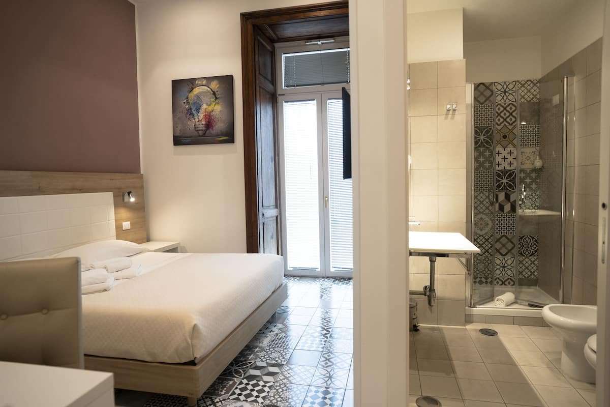 A modern hotel room with a bed, bedside table, and a shower area with a glass door.
