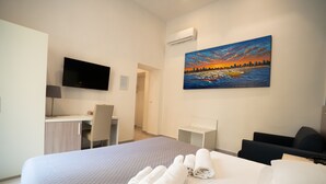 Hotellihuone, jossa on sänky, työpöytä, tuoli, televisio ja taulu seinällä.