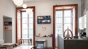 Moderni hotellihuone, jossa on ruokailutila, televisio, jolta näkyy elokuva, ja näkymä kaupunkiin.