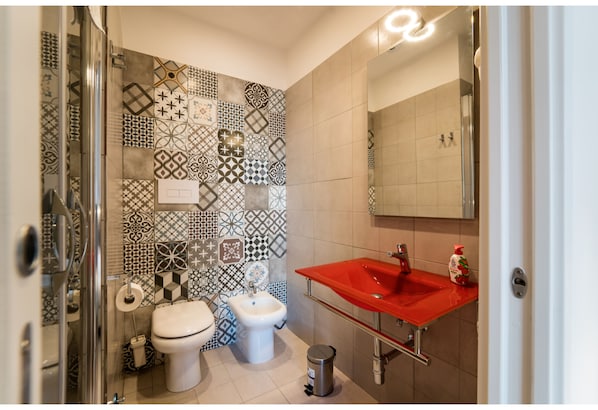 Une salle de bain avec des carreaux décorés, des toilettes blanches, un bidet et un lavabo rouge.