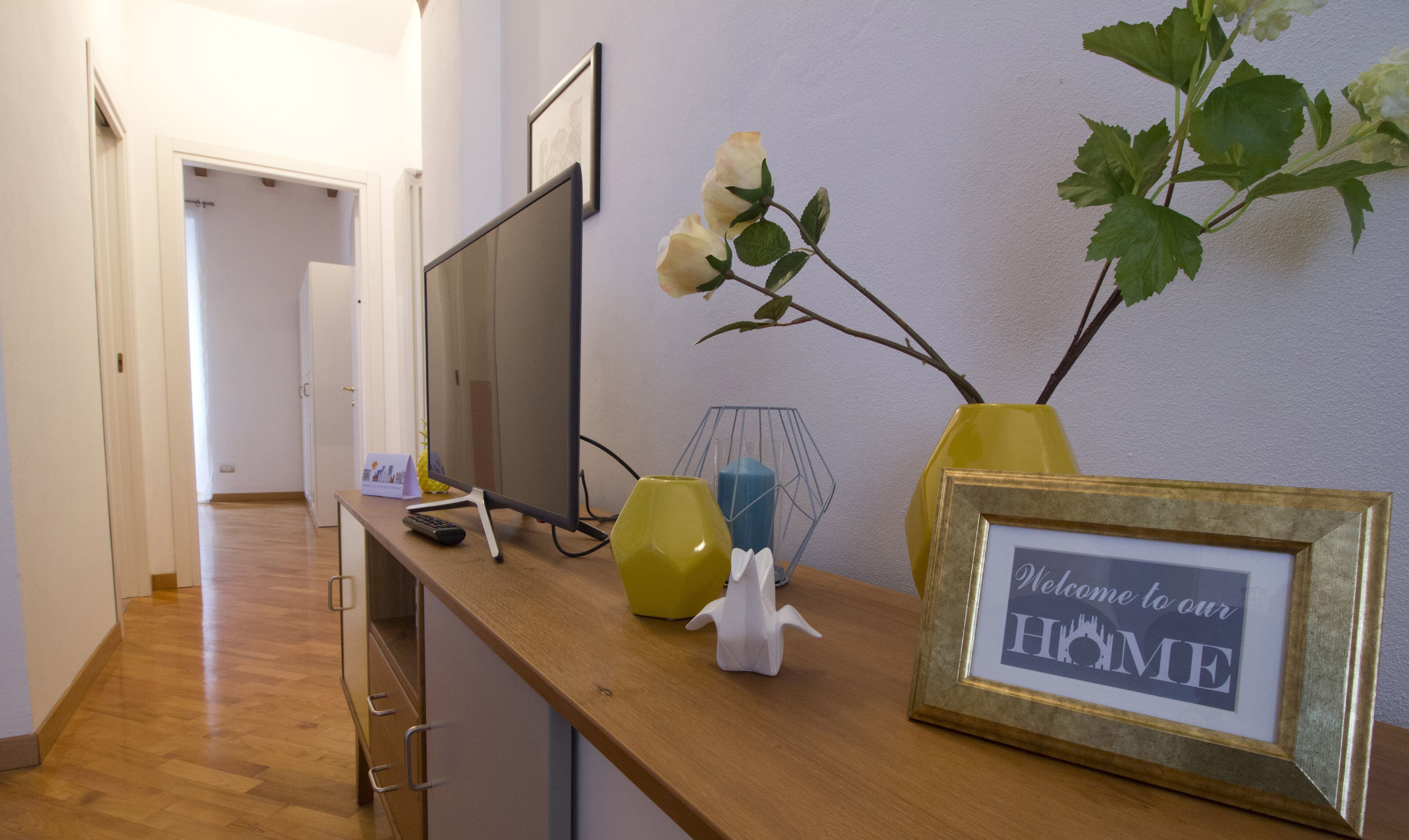 A reception desk with a framed welcome sign, a vase with a plant, and a remote control.