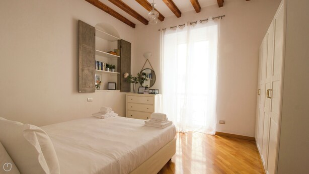 Une chambre à coucher avec un lit, une commode, un miroir et une fenêtre avec des rideaux.