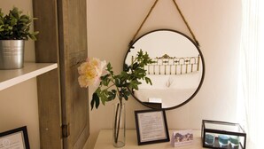 Une pièce avec un miroir rond, un vase avec une fleur, un panneau d’accueil encadré et un panneau indiquant qu’il est interdit de fumer.