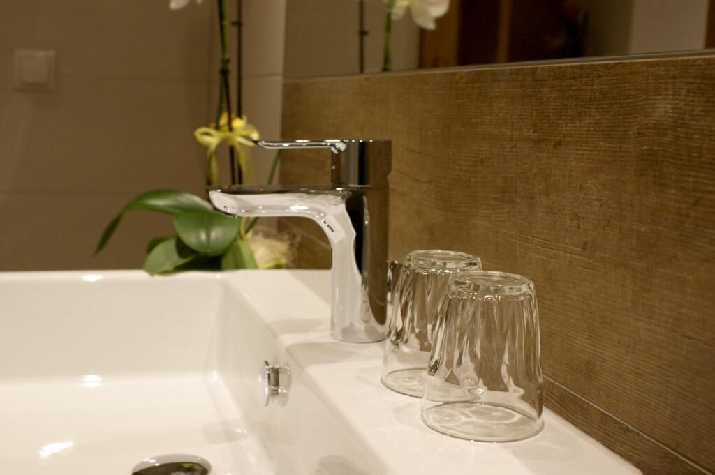 A bathroom sink with a chrome faucet and three clear glasses on the counter.