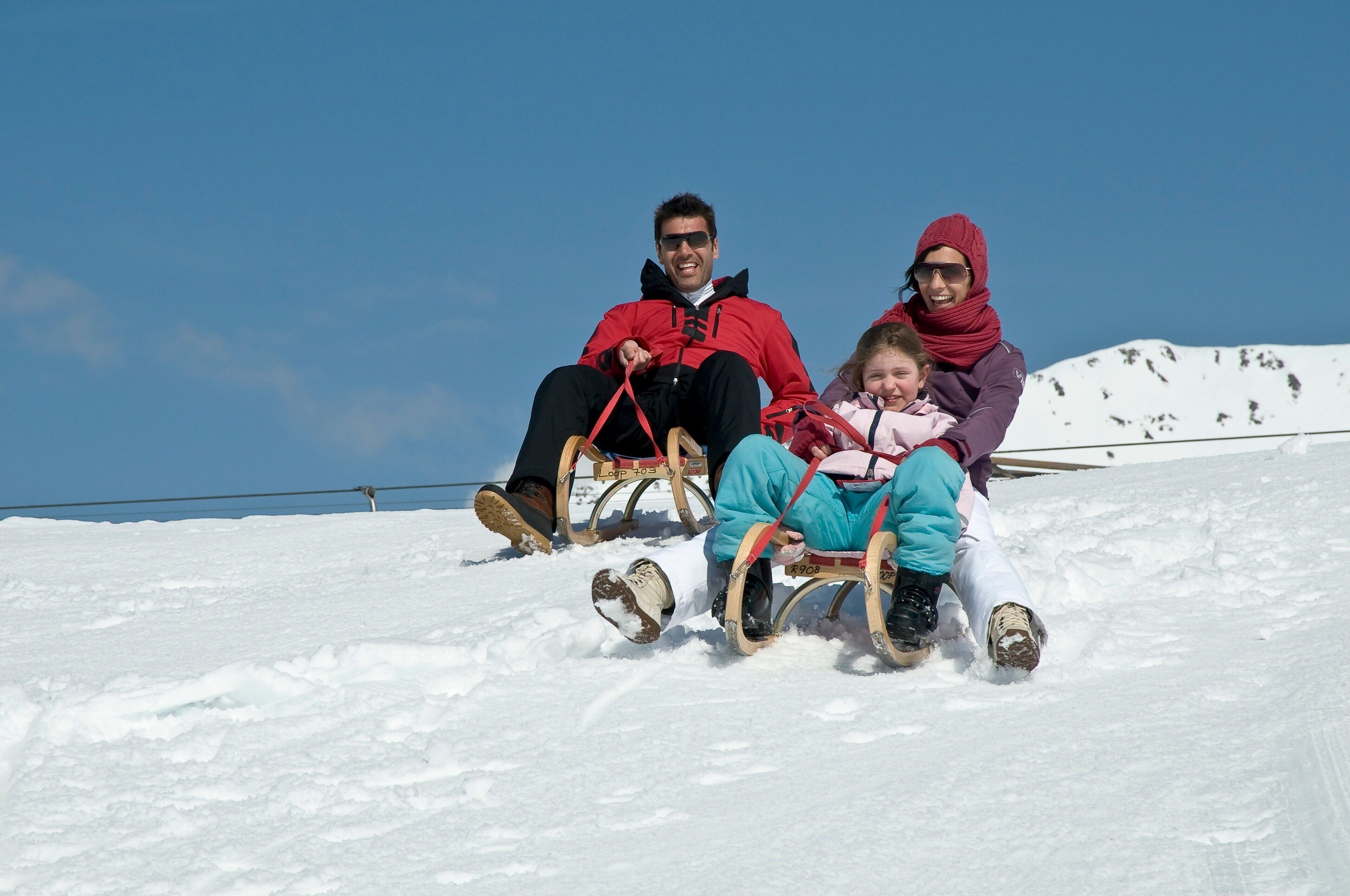 Three people sledding down a snowy slope.