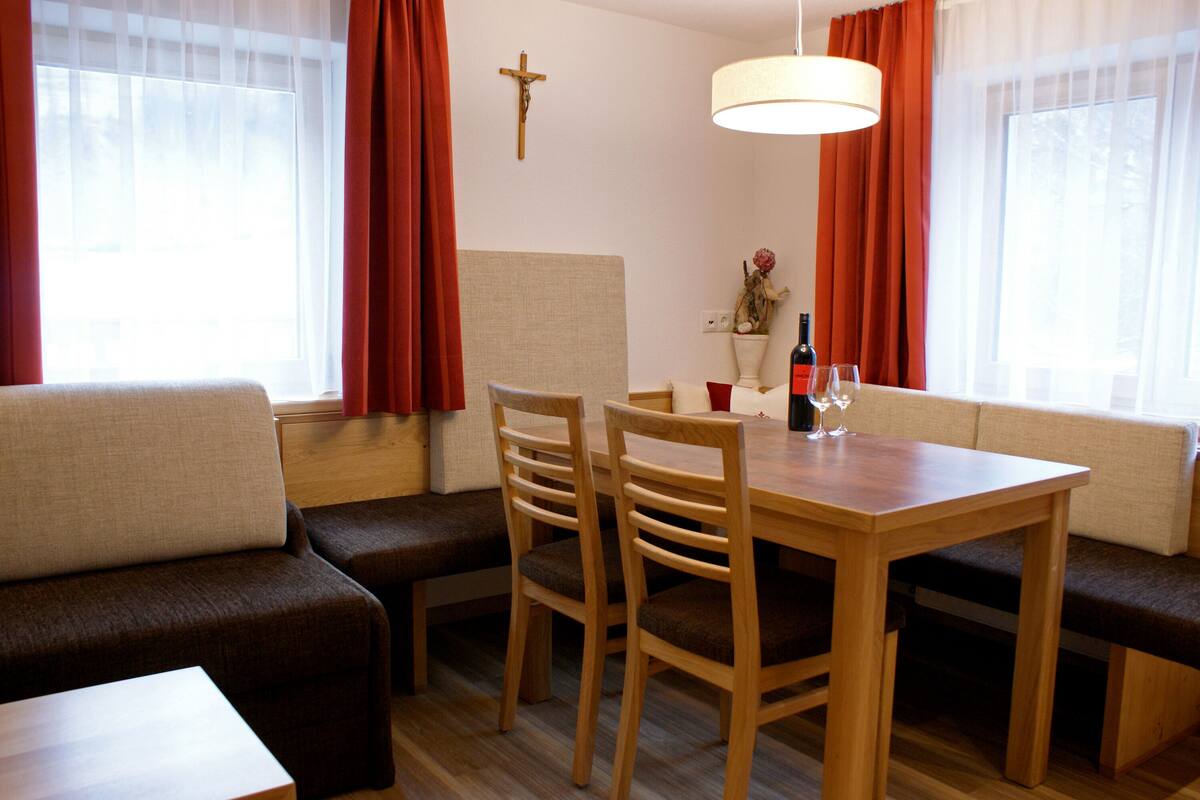 A dining area with a wooden table, four chairs, a bench, and a cross on the wall.