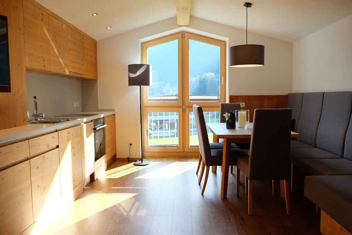 A modern kitchen with wooden cabinets, a dining area with a table and chairs, and a large window providing natural light.