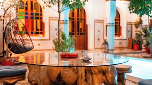 A round glass table with a wooden base, surrounded by chairs, in a courtyard with a building in the background. - Ysalis Riad Restaurant & Spa (Marrakech)