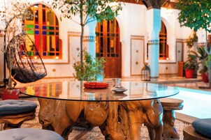 Una mesa redonda de vidrio con base de madera, rodeada de sillas, en un patio con un edificio al fondo.