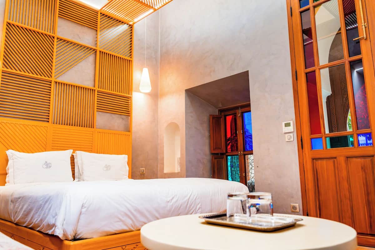 A hotel room with a bed, a round table with a glass, and a wooden cabinet with glass doors.