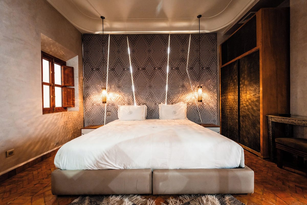 A modern bedroom with a large bed, patterned wallpaper, and a unique light fixture.