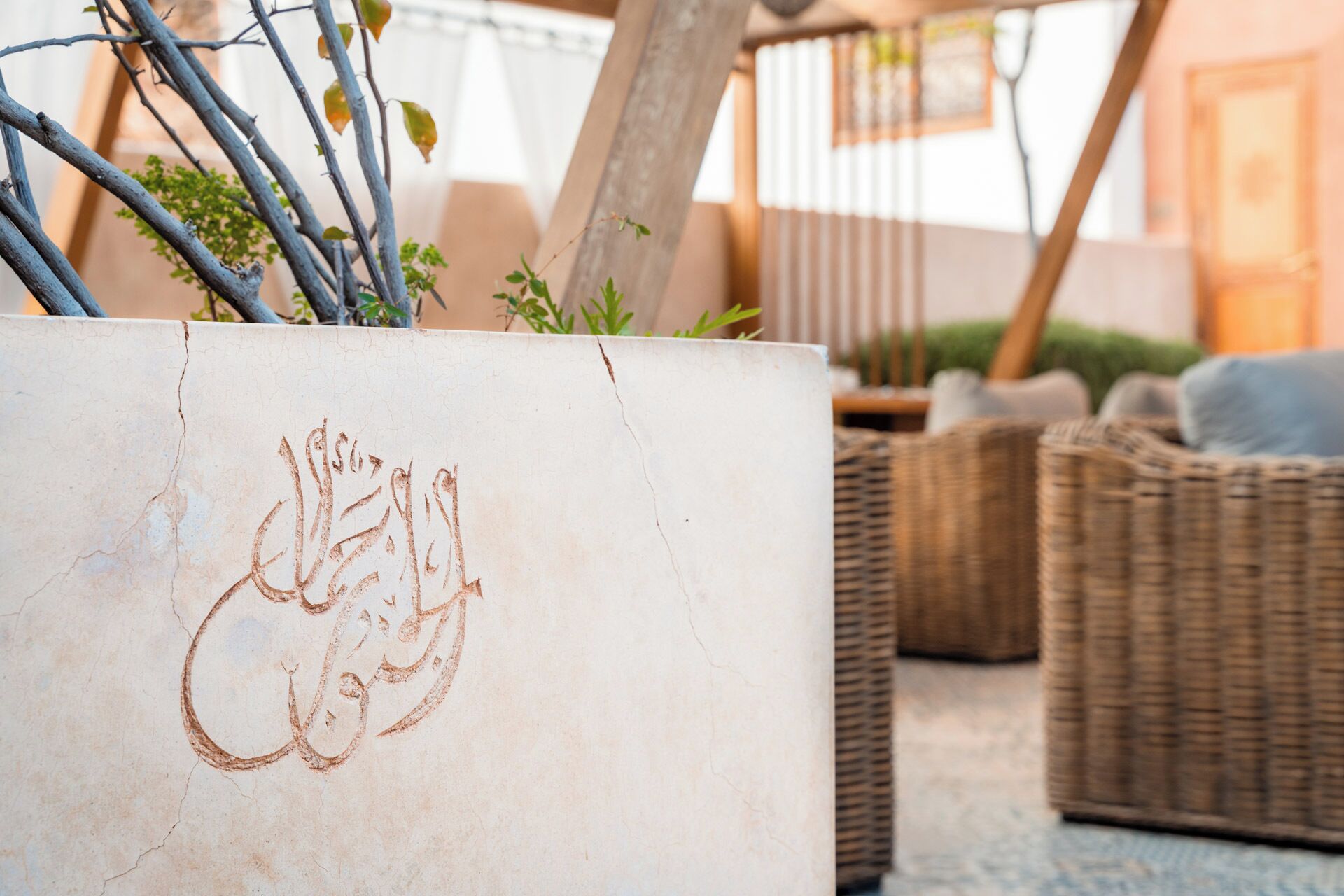 A white planter with Arabic calligraphy, wicker furniture, and a hammock in a cozy outdoor setting.