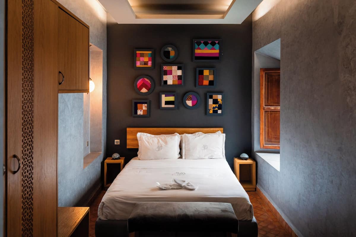 A modern hotel room with a large bed, a wooden headboard, and a wall decorated with framed artwork.