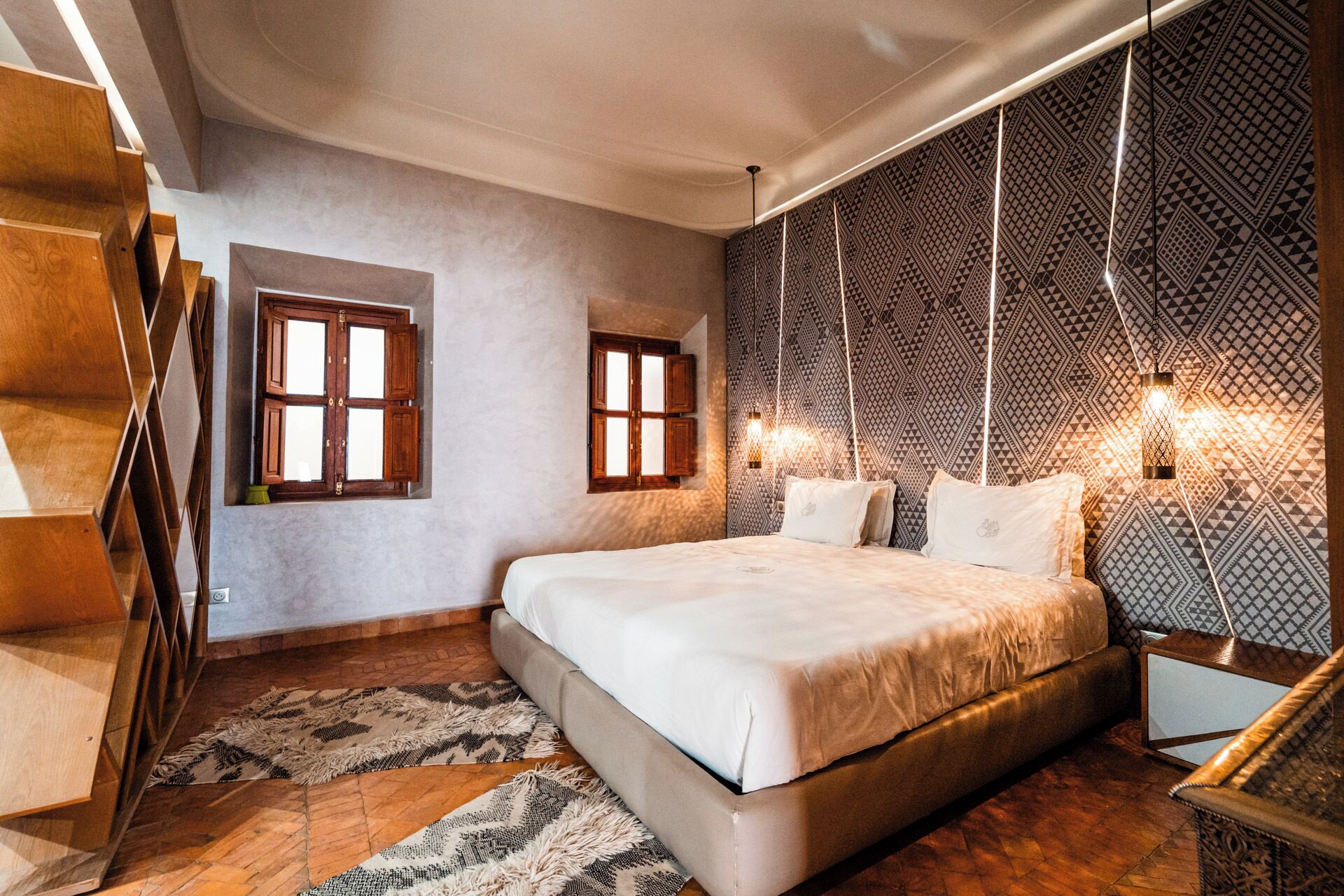 A bedroom with a large bed, two windows, patterned wallpaper, and a staircase.