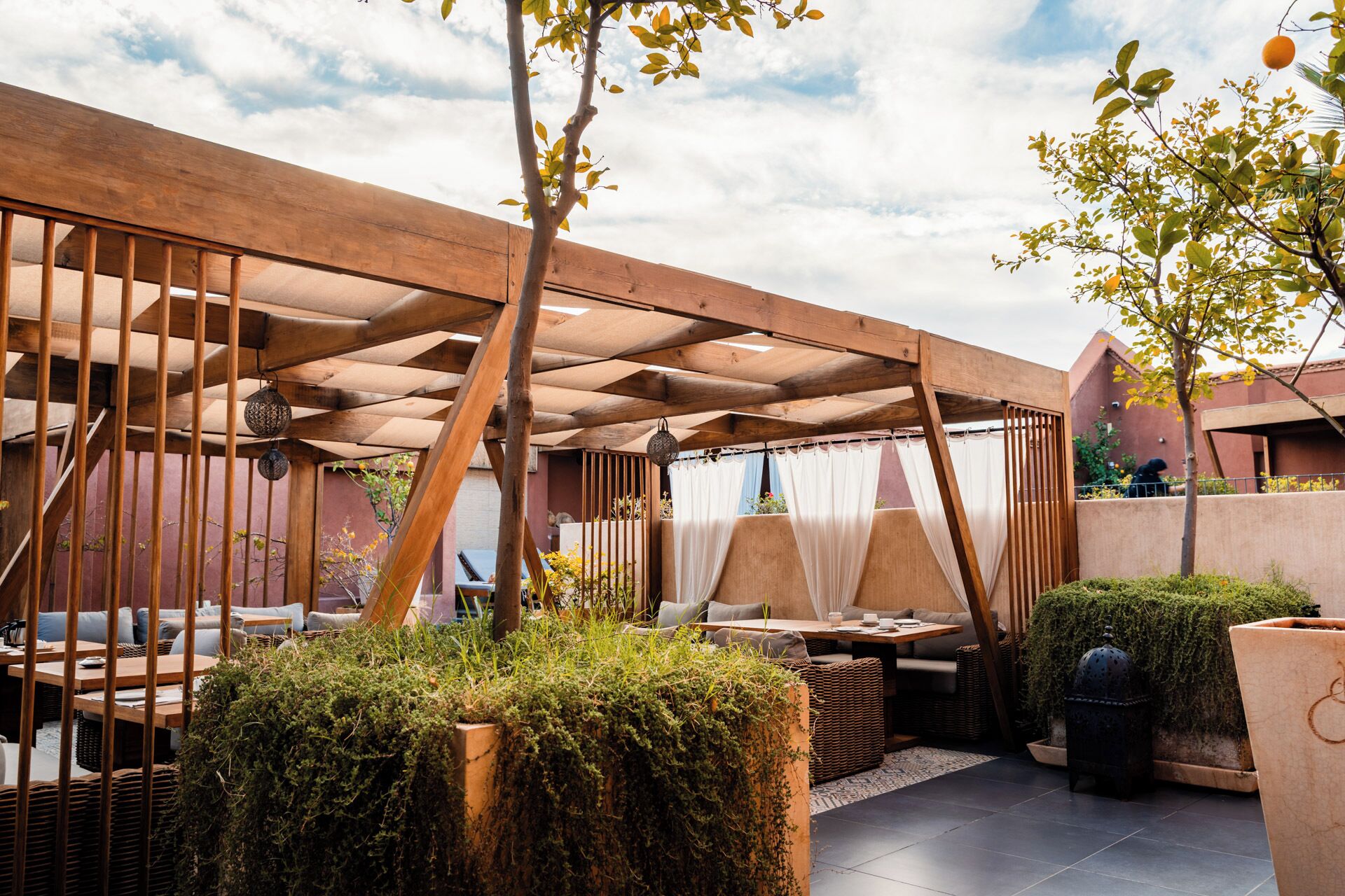 Un espacio al aire libre con pérgolas de madera, asientos acolchados y plantas en macetas.