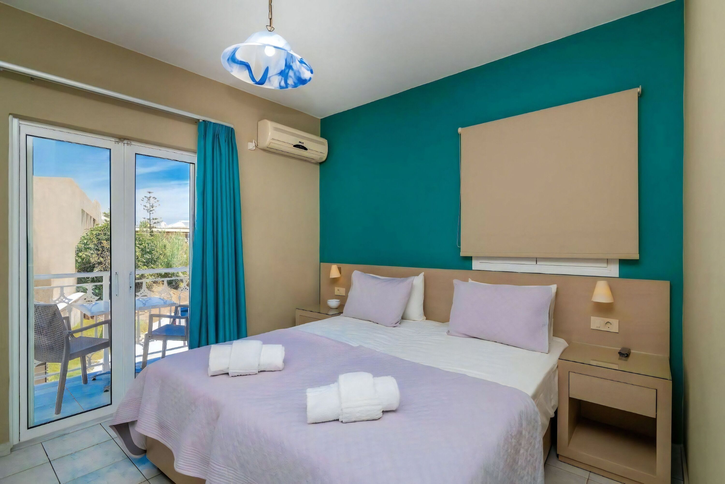 Habitación de hotel con cama, mesita de noche, ventana con cortinas, equipo de aire acondicionado y vista al exterior.