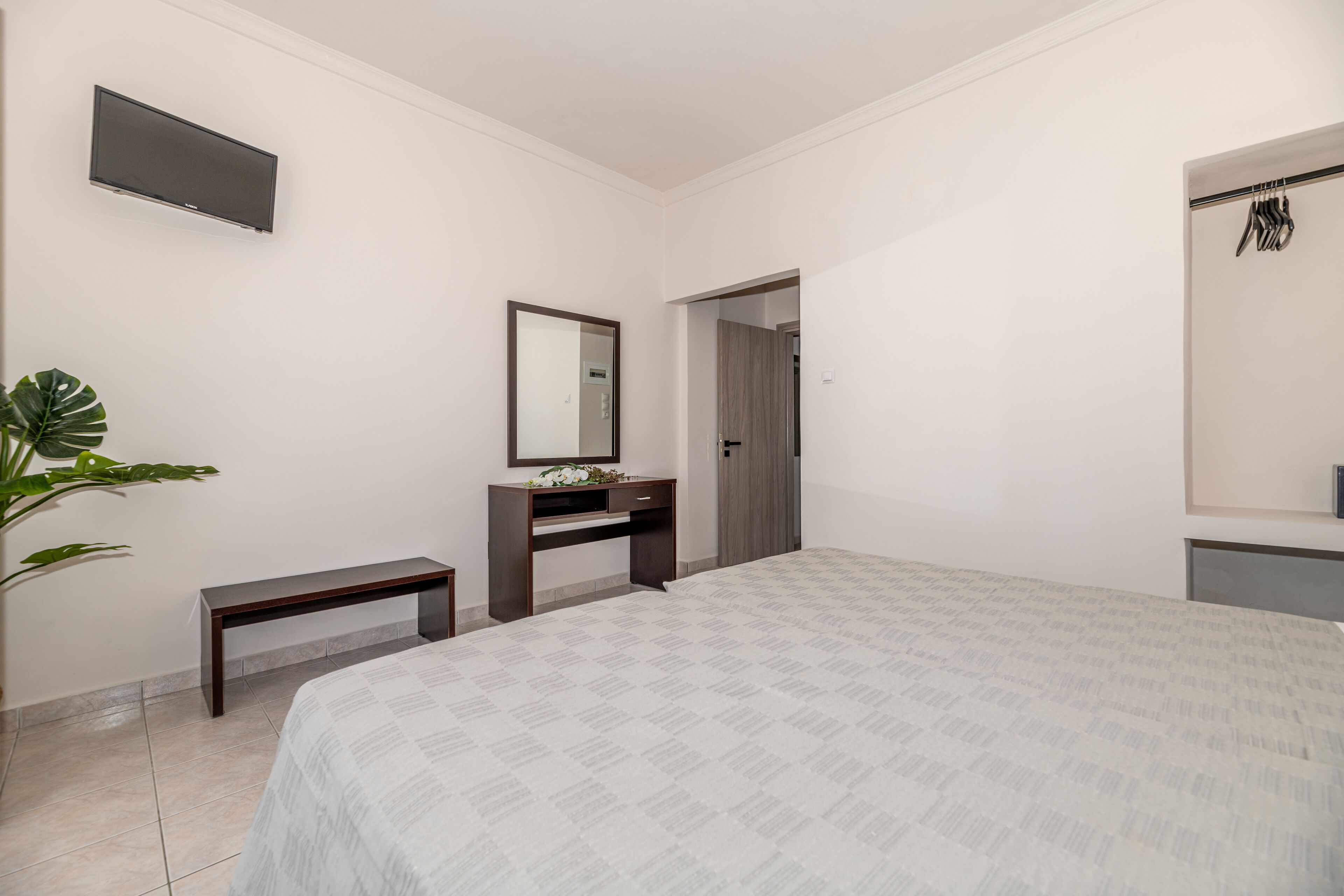 A bedroom with a bed, a dresser, a mirror, a TV, and a door leading to another room.