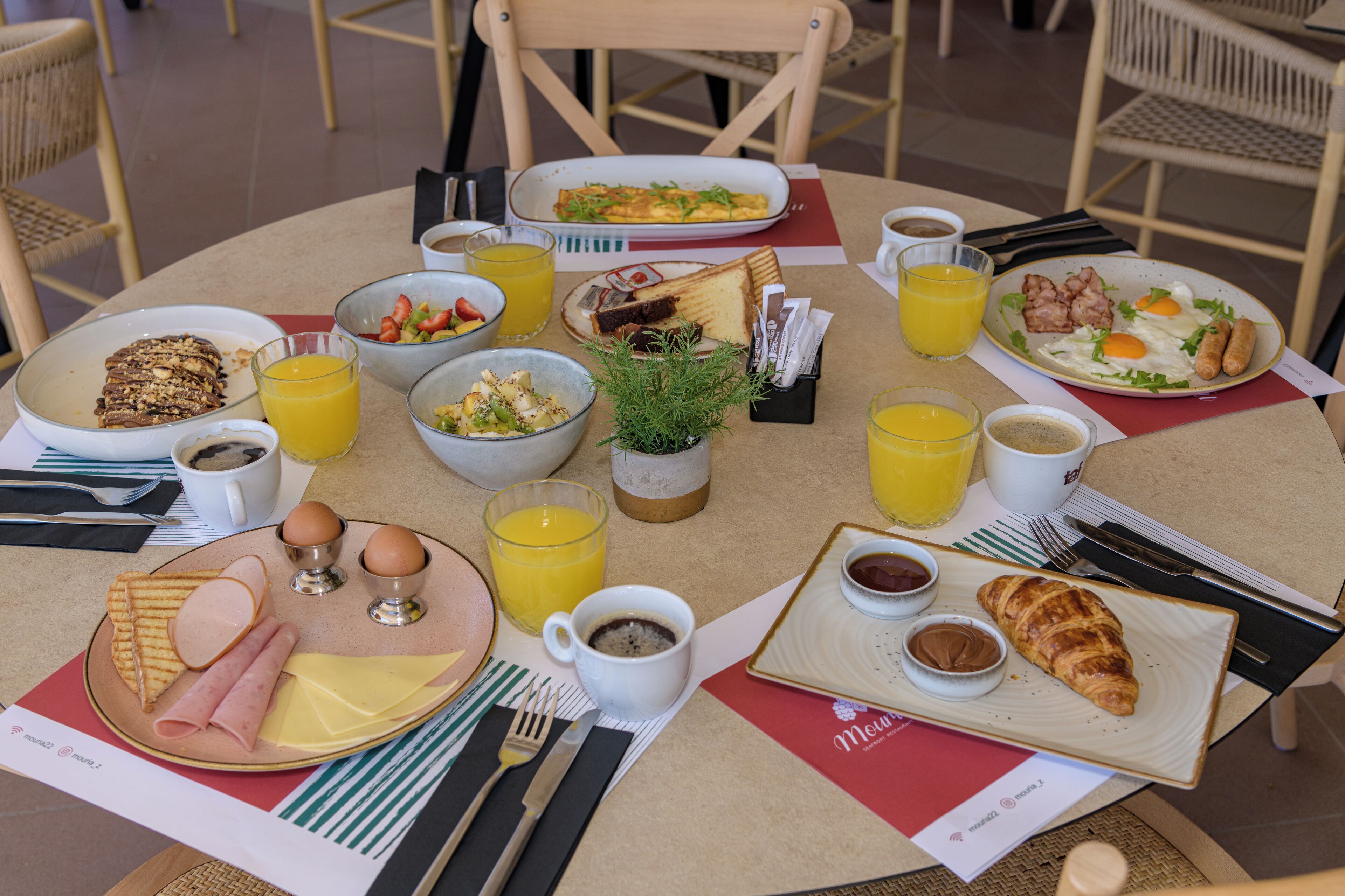 Une table dressée pour le petit-déjeuner, avec différents plats, notamment des œufs, du bacon, des toasts et du jus de fruits.