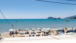 A beach with umbrellas and lounge chairs, a clear sky, and boats in the water. - Mouria Studios & Apartments (Zakynthos)