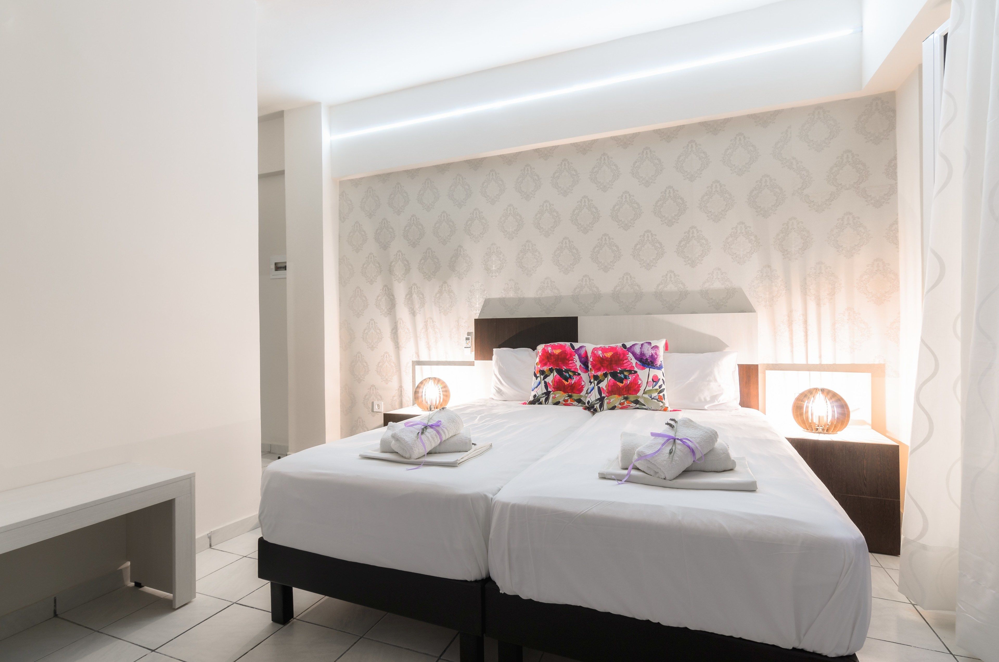 Une chambre d’hôtel avec deux lits, une table de chevet avec une lampe et un banc.
