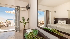 A hotel room with a bed, a large mirror, a balcony with a table and chairs, and a view of the sea. - Mouria Studios & Apartments (Zakynthos)