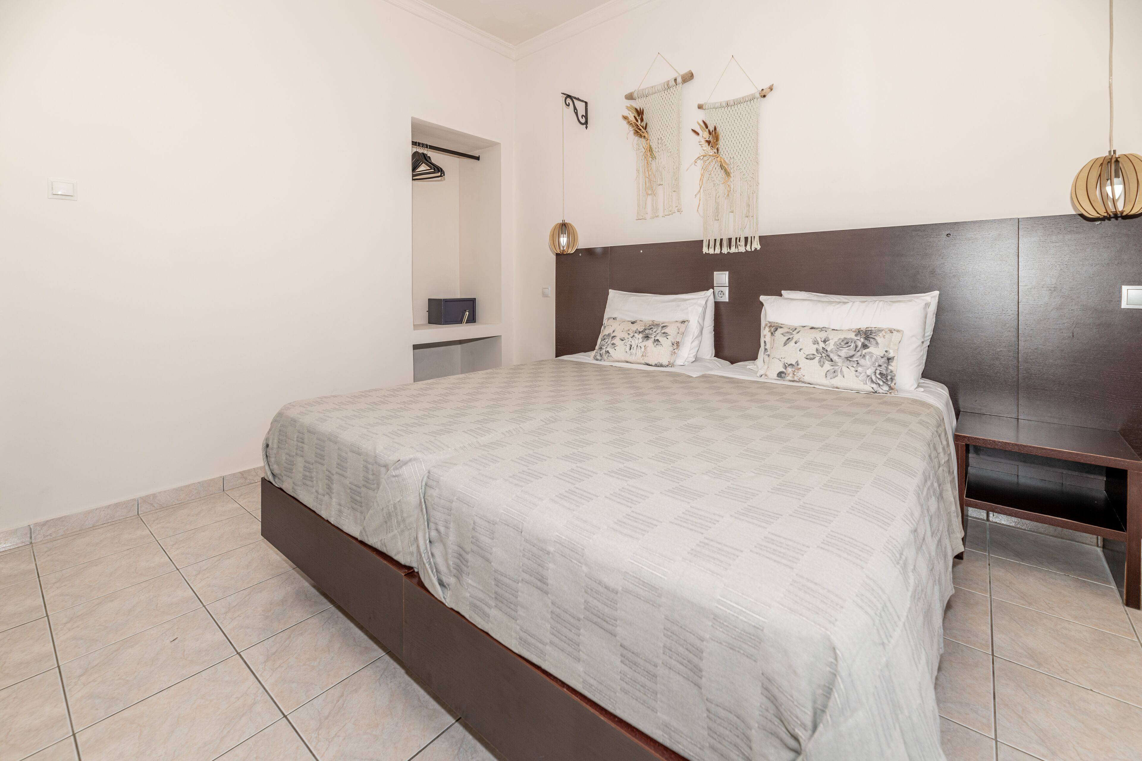 A bedroom with a large bed, a wooden headboard, a bedside table, a wardrobe, and a wall-mounted light fixture.