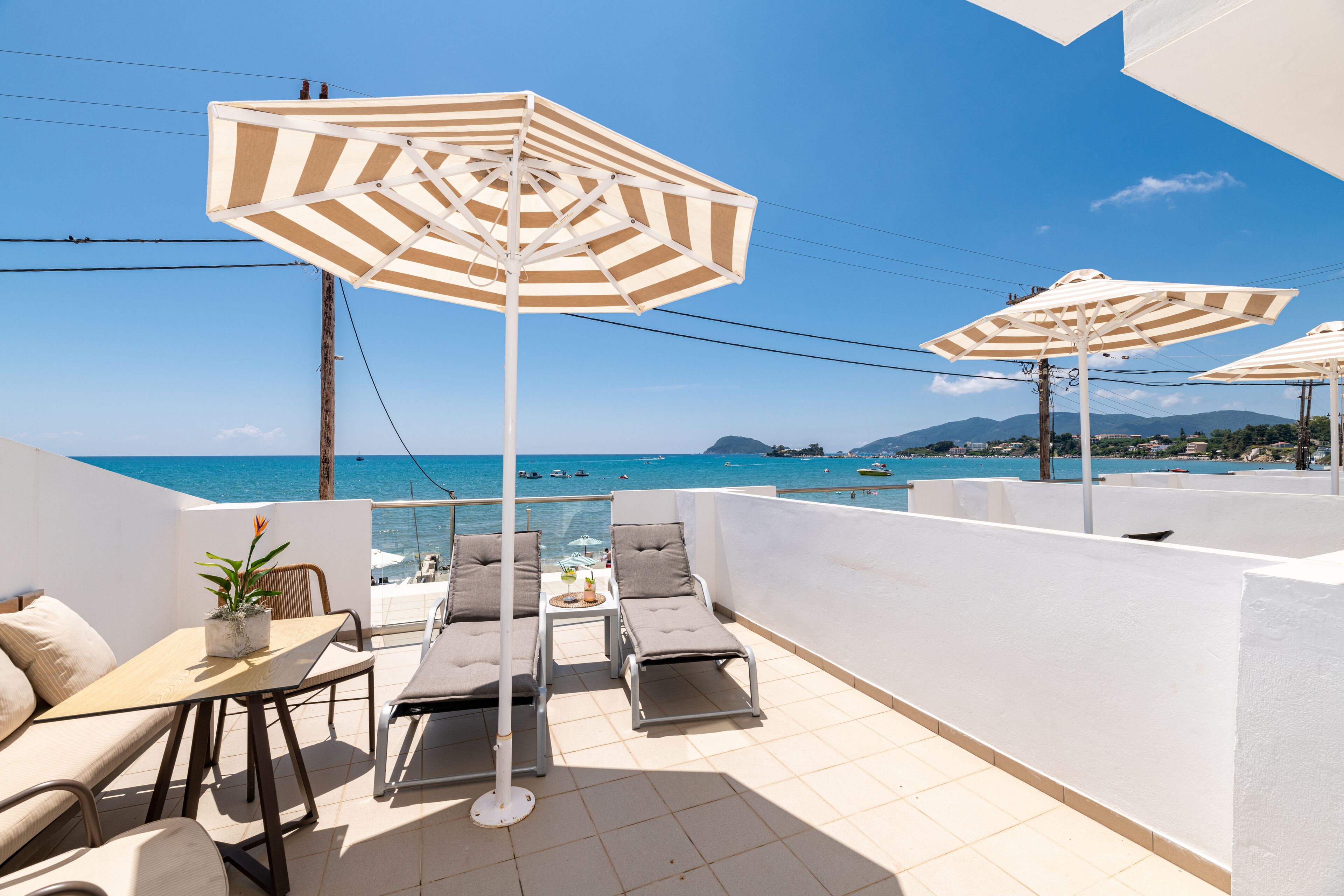 Un balcon avec deux fauteuils, une table et des parasols à rayures.