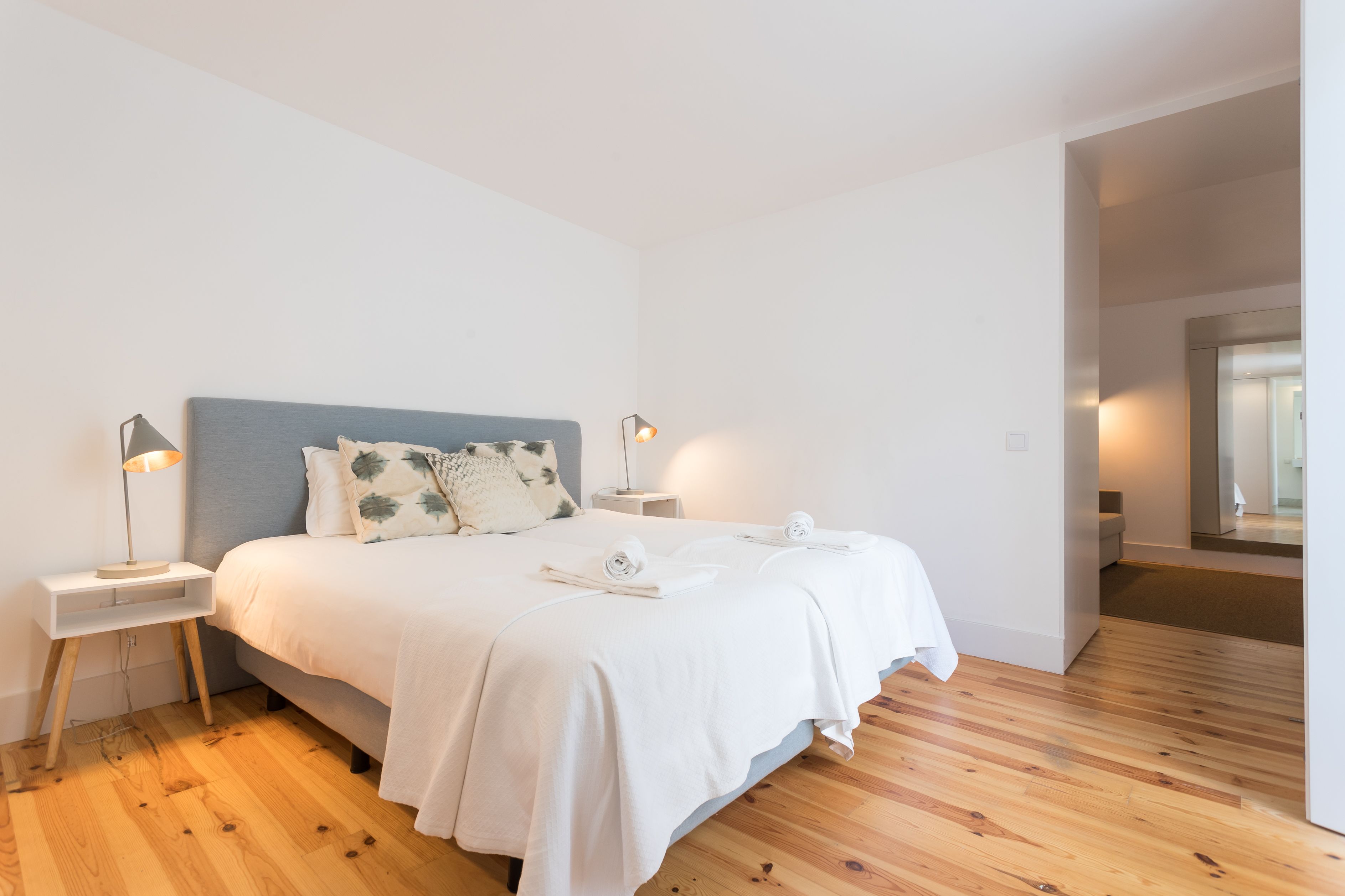 A modern bedroom with a large bed, wooden flooring, and bedside lamps.