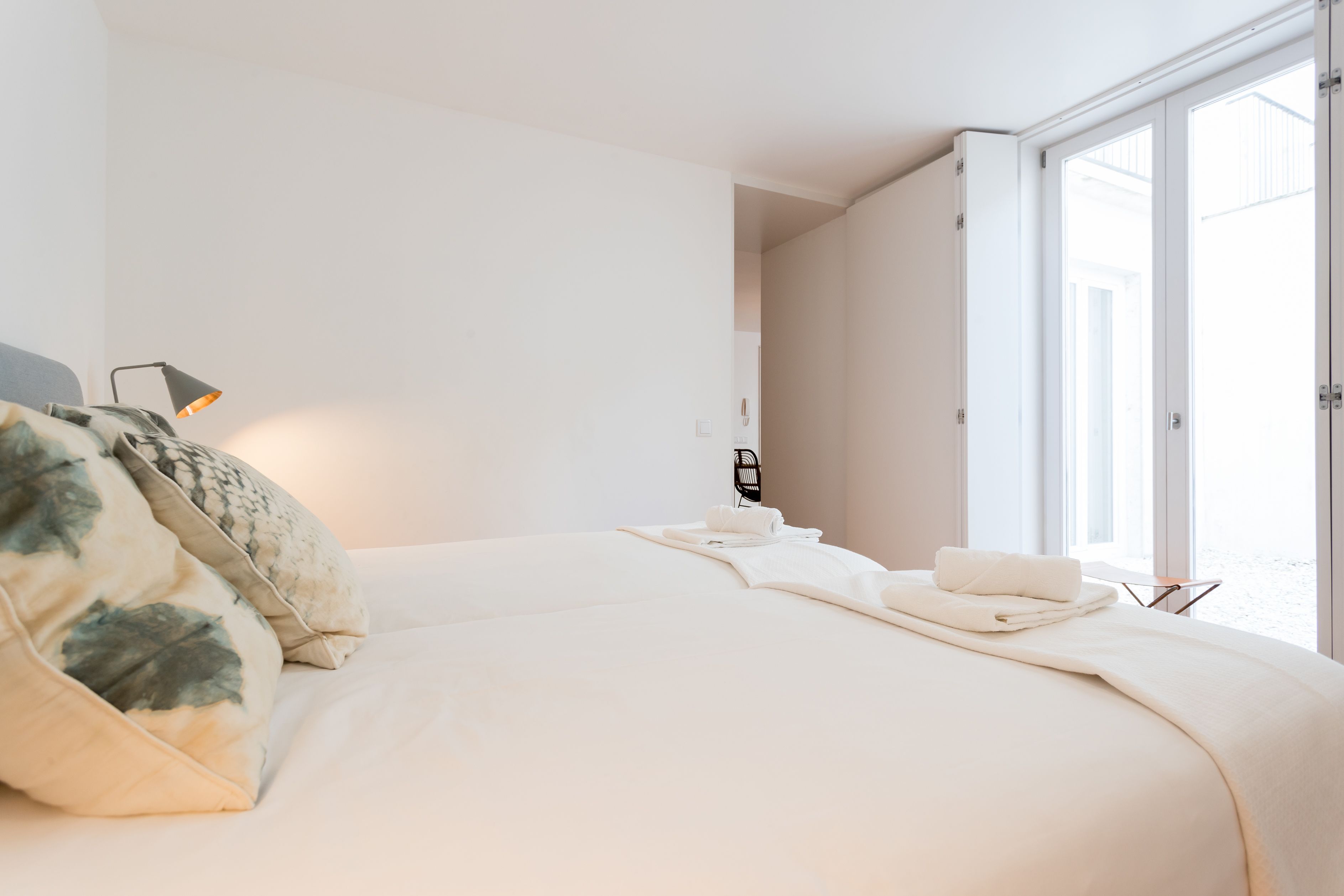 Une chambre d’hôtel au design minimaliste, dotée d’un grand lit, d’une table de chevet, d’une lampe et offrant une vue sur l’extérieur grâce à une porte coulissante.