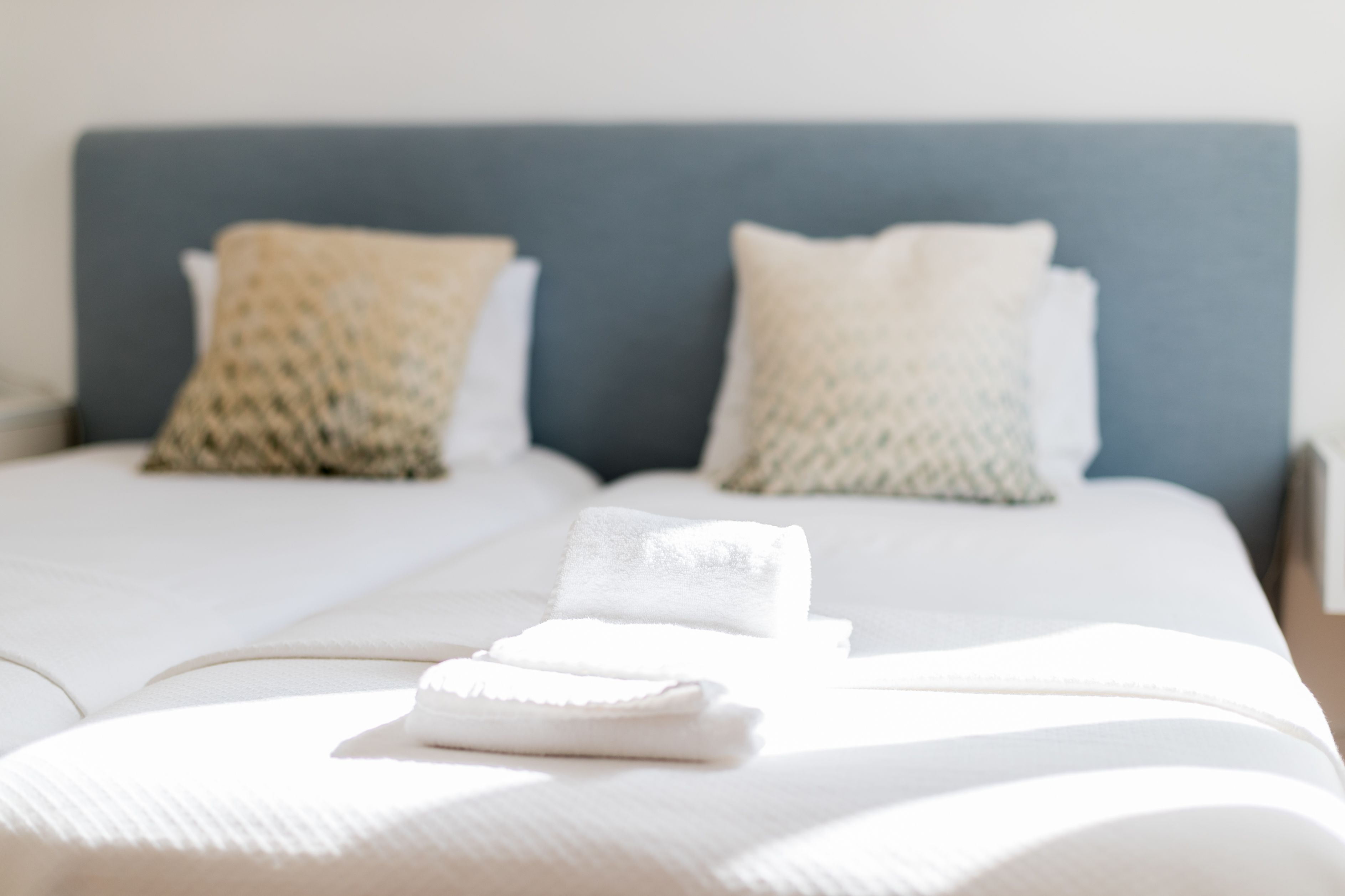 A neatly made bed with white linens and two pillows, one with a patterned cover and the other plain.