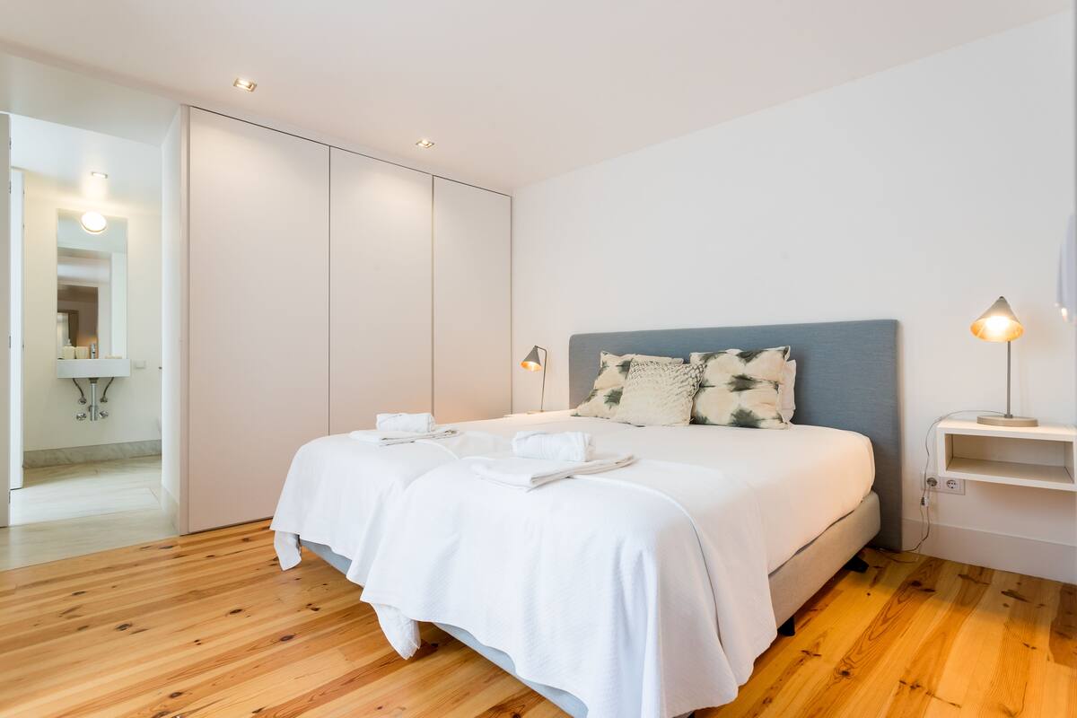 A modern bedroom with a large bed, white linens, and a wooden floor.