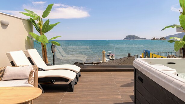 Uma varanda com vista para o mar, espreguiçadeiras, banheira de hidromassagem e um deck de madeira.
