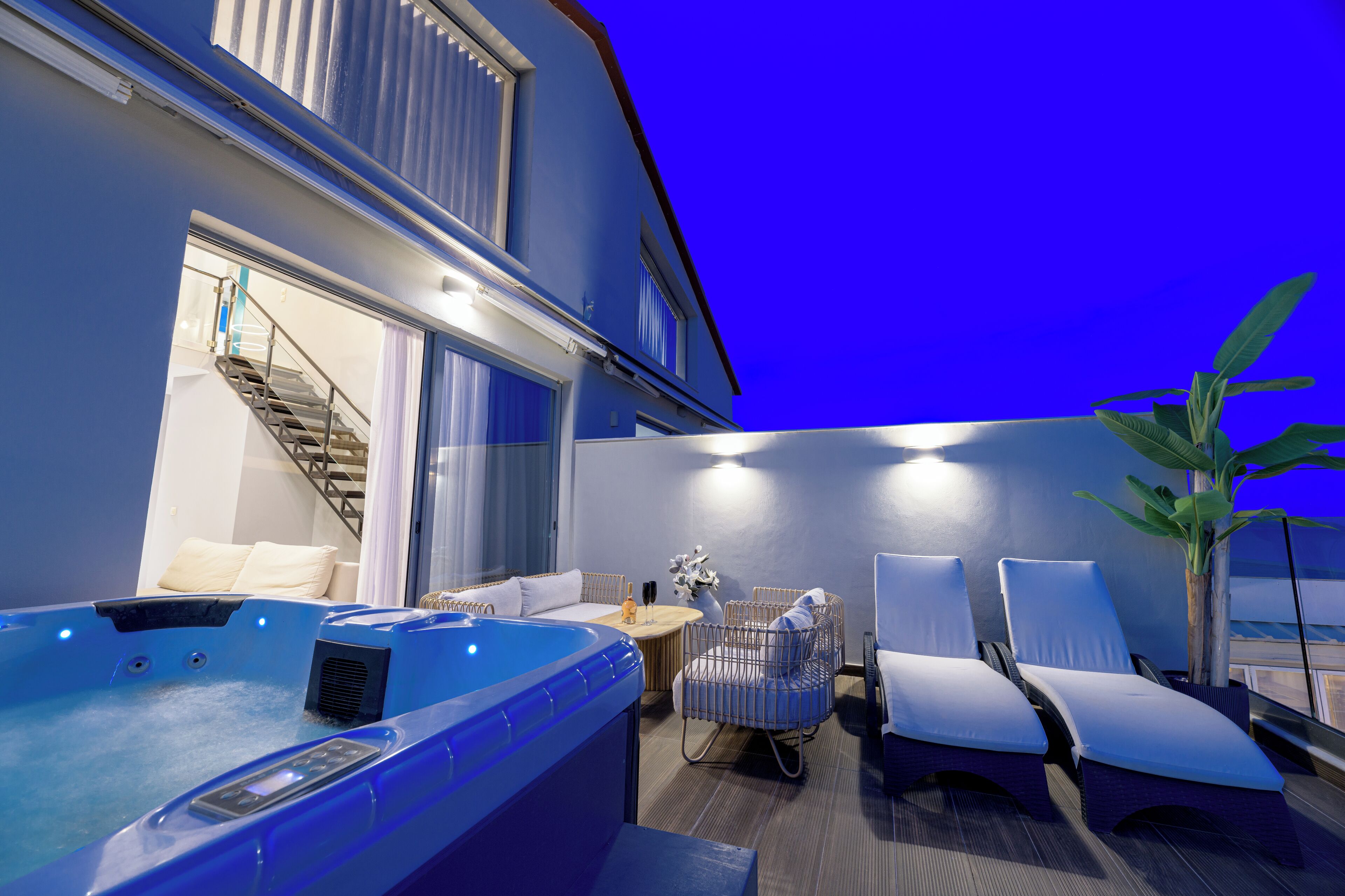 A modern indoor pool area with a hot tub, lounge chairs, and a staircase leading to an upper level.