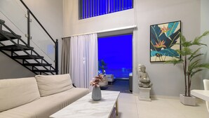 Uma sala de estar moderna com um sofá, uma mesa de centro, uma escada, uma estátua de Buda e um quadro.