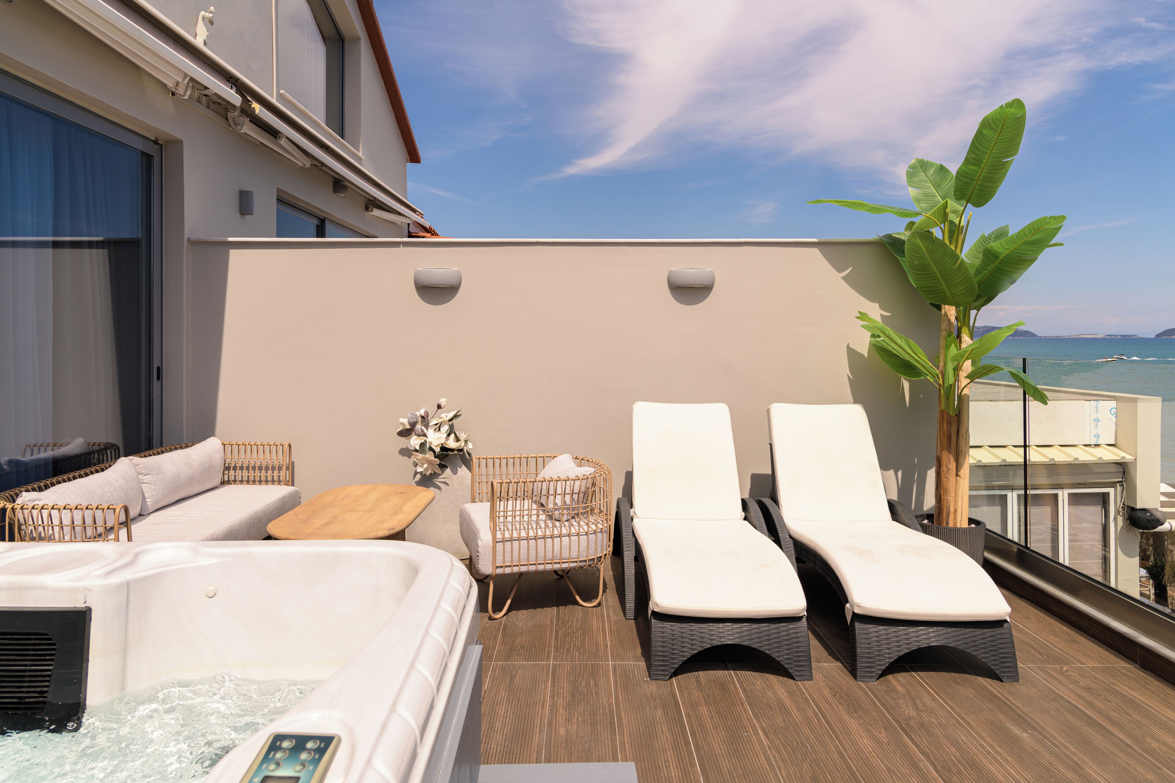 A rooftop terrace with a hot tub, lounge chairs, a wicker sofa, and a potted plant.