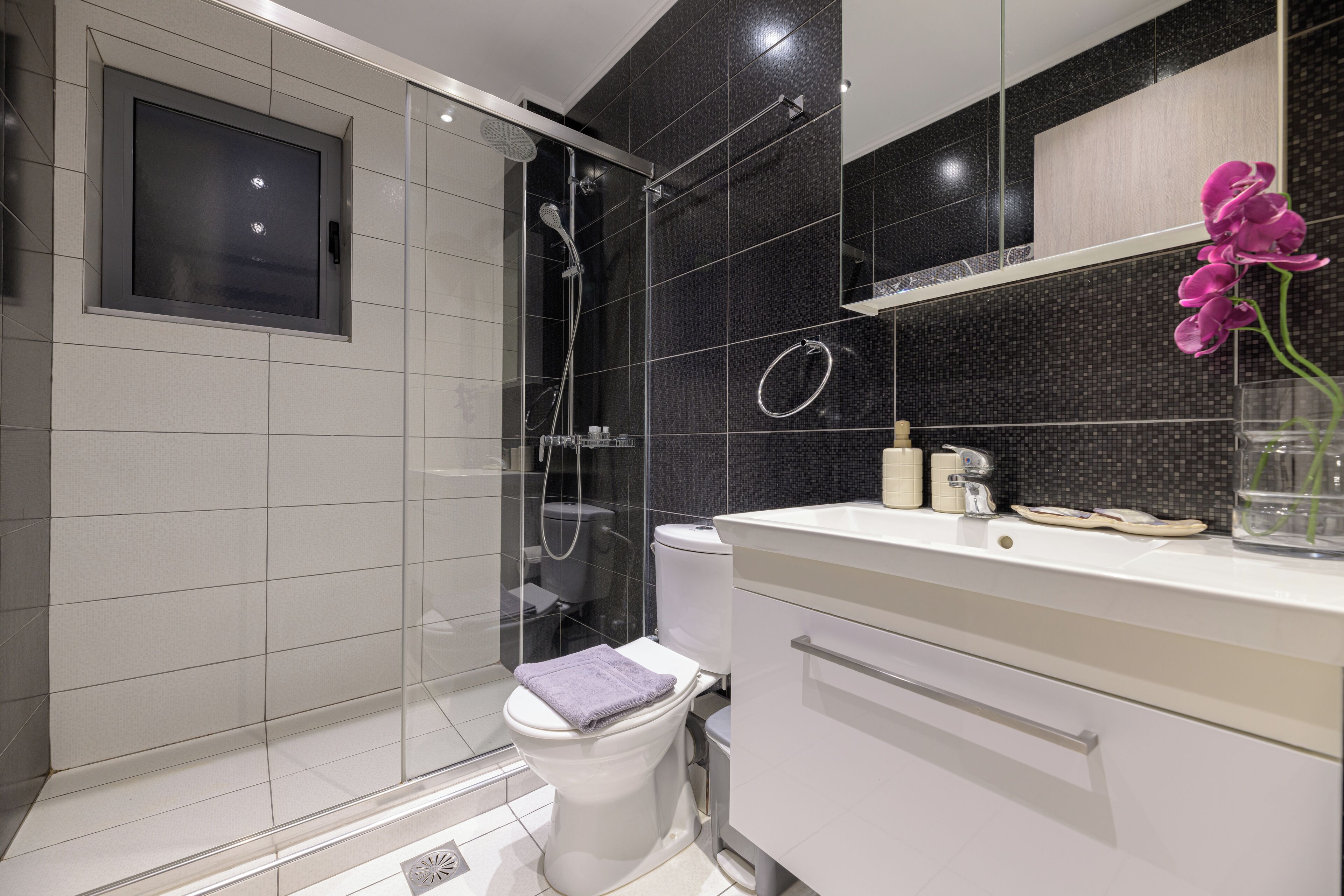 A modern bathroom with a glass-enclosed shower, a toilet, and a vanity with a mirror.
