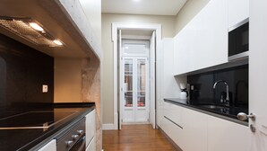 A narrow kitchen with a black countertop, white cabinets, and a wooden floor.