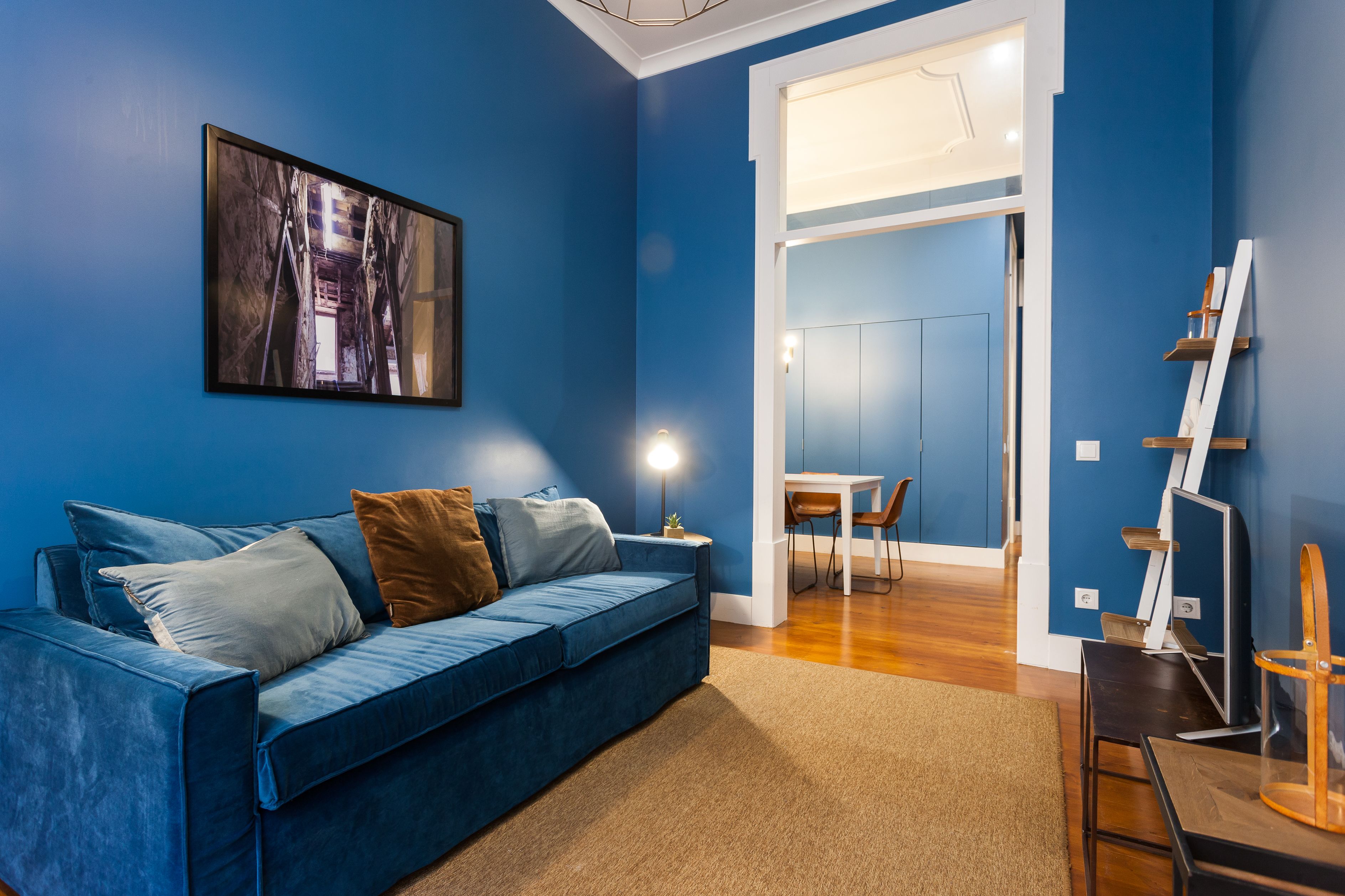 Ein modernes Wohnzimmer mit einem blauen Sofa, einem Gemälde und einem Essbereich mit Tisch und Stühlen.