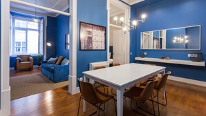 A modern living room with a blue accent wall, a white dining table, and brown chairs.