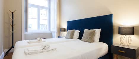 A hotel room with two beds, a window, a lamp, and a nightstand.