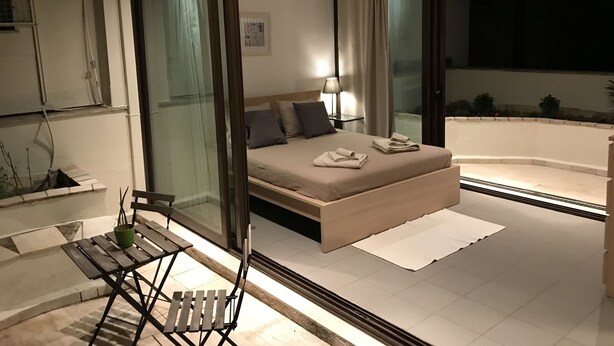 Quarto moderno com uma cama grande, mesa de cabeceira com abajur e vista para o exterior.