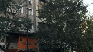 Um edifício de vários andares com aparelhos de ar condicionado, uma loja com sinalização e uma rua em frente.