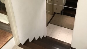 Uma escadaria leva a um espaço com vaso sanitário, armário e uma porta com cortina branca.