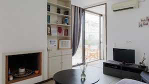 Sala de estar moderna com lareira, televisão e zona de refeições visível através de uma porta de vidro.