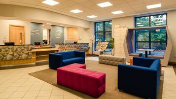 A reception area with a counter, blue and pink seating, a bulletin board, and large windows.