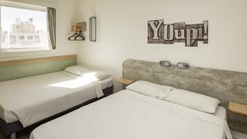 Quarto de hotel com duas camas, uma janela com cortinas, prateleira na parede com um relógio e um aviso com a inscrição 'Youpi!'.