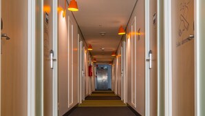 A hotel corridor with doors on both sides, overhead lighting, and a fire extinguisher on the left wall.