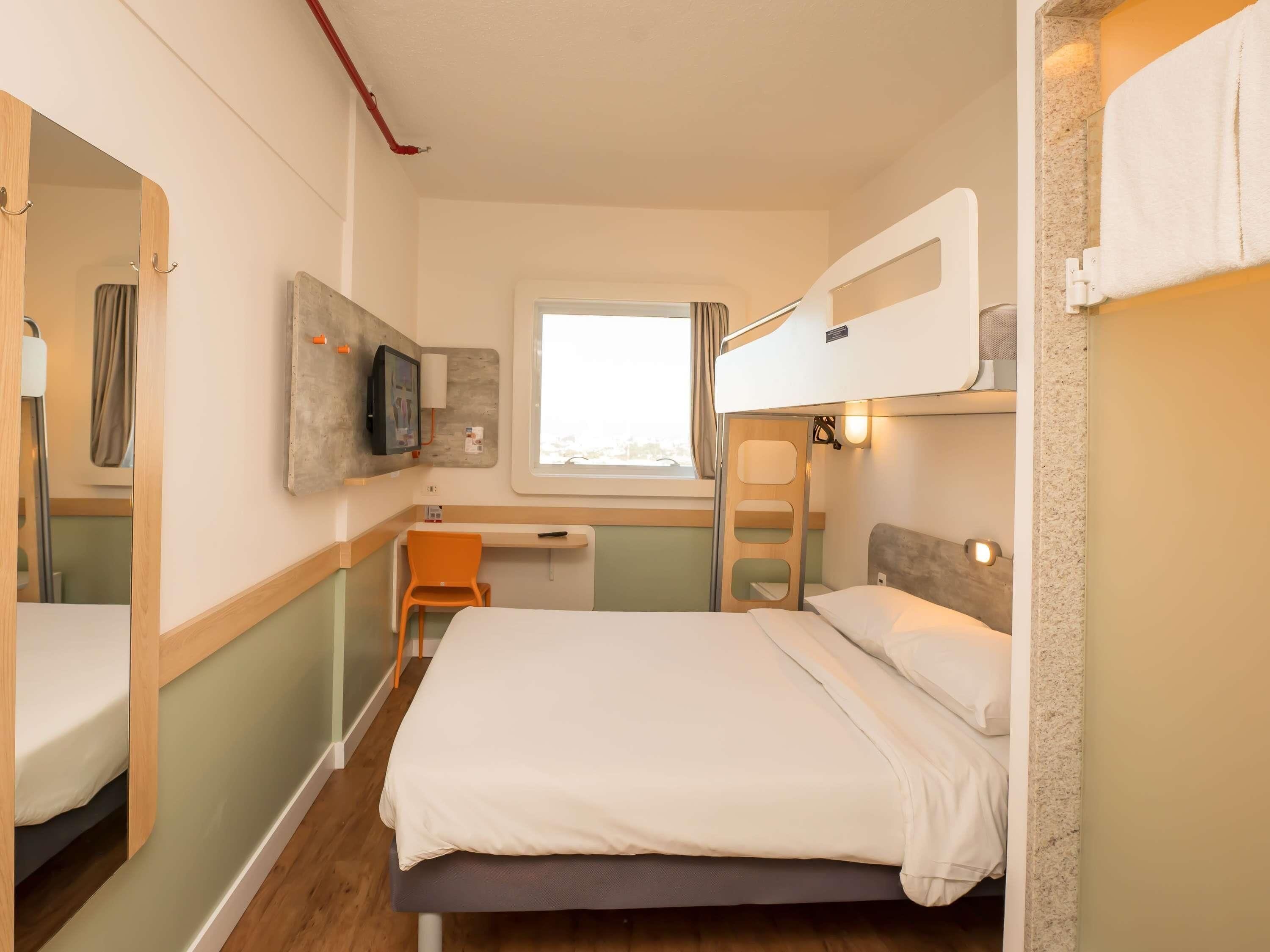Habitación de hotel compacta con literas, un escritorio, una silla, un televisor y una ventana.