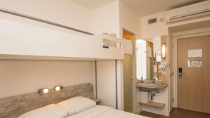 A hotel room with a bed, a bedside table, a mirror, a sink, and a door.