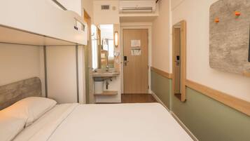 A hotel room with a bunk bed, a bathroom with a sink, mirror, and towel dispenser, and a door leading to another room.